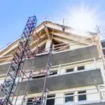 Apartment building under construction seen from below Apartment building under construction. Behind the house you can see clear blue sky and the sun that is shining and creates sunbeams. Concept of good times with wellfare, booms and development for the construction industry and population growth.