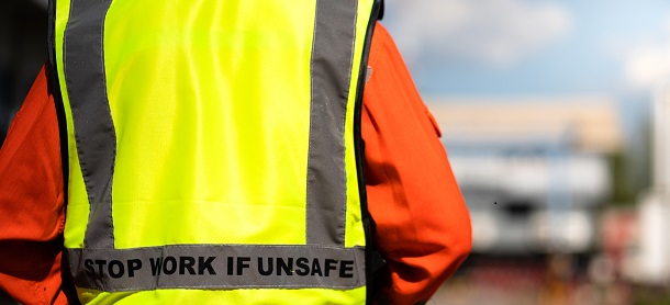 Close-up at "Stop work if unsafe" sign label on back of reflective vest which is wear by a lifting signaler worker. Safety conception photo for heavy industry operation.